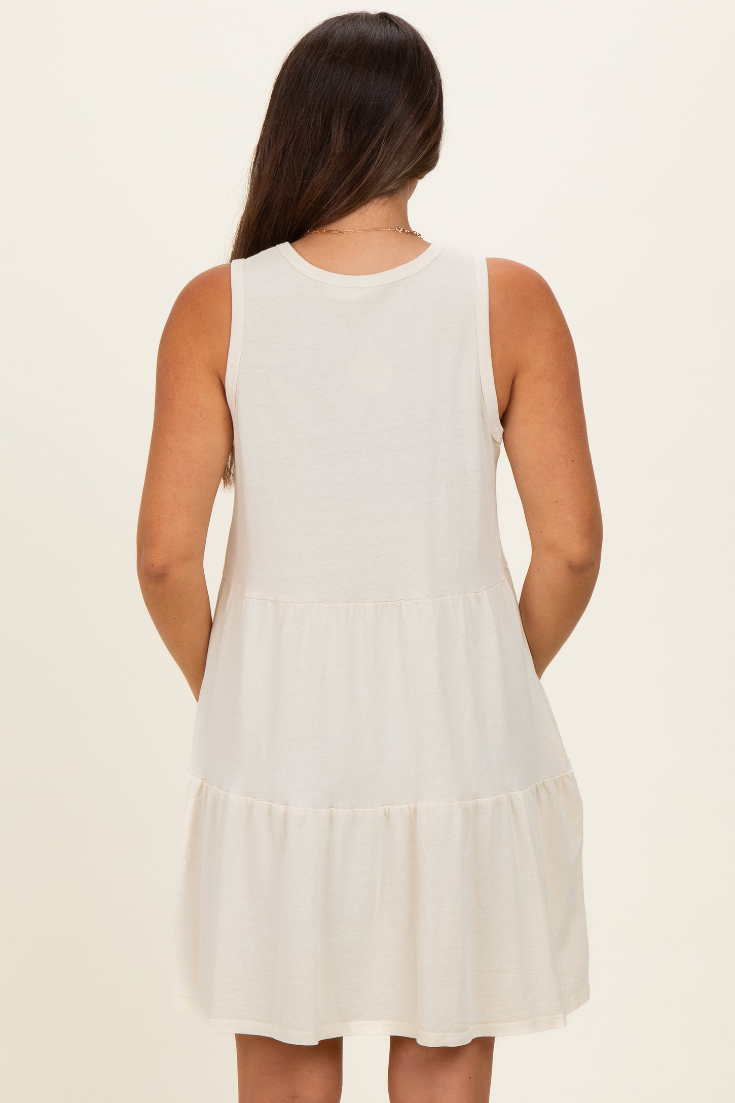 woman wearing a cream maternity dress with a tiered skirt and a sleeveless design, showing her back