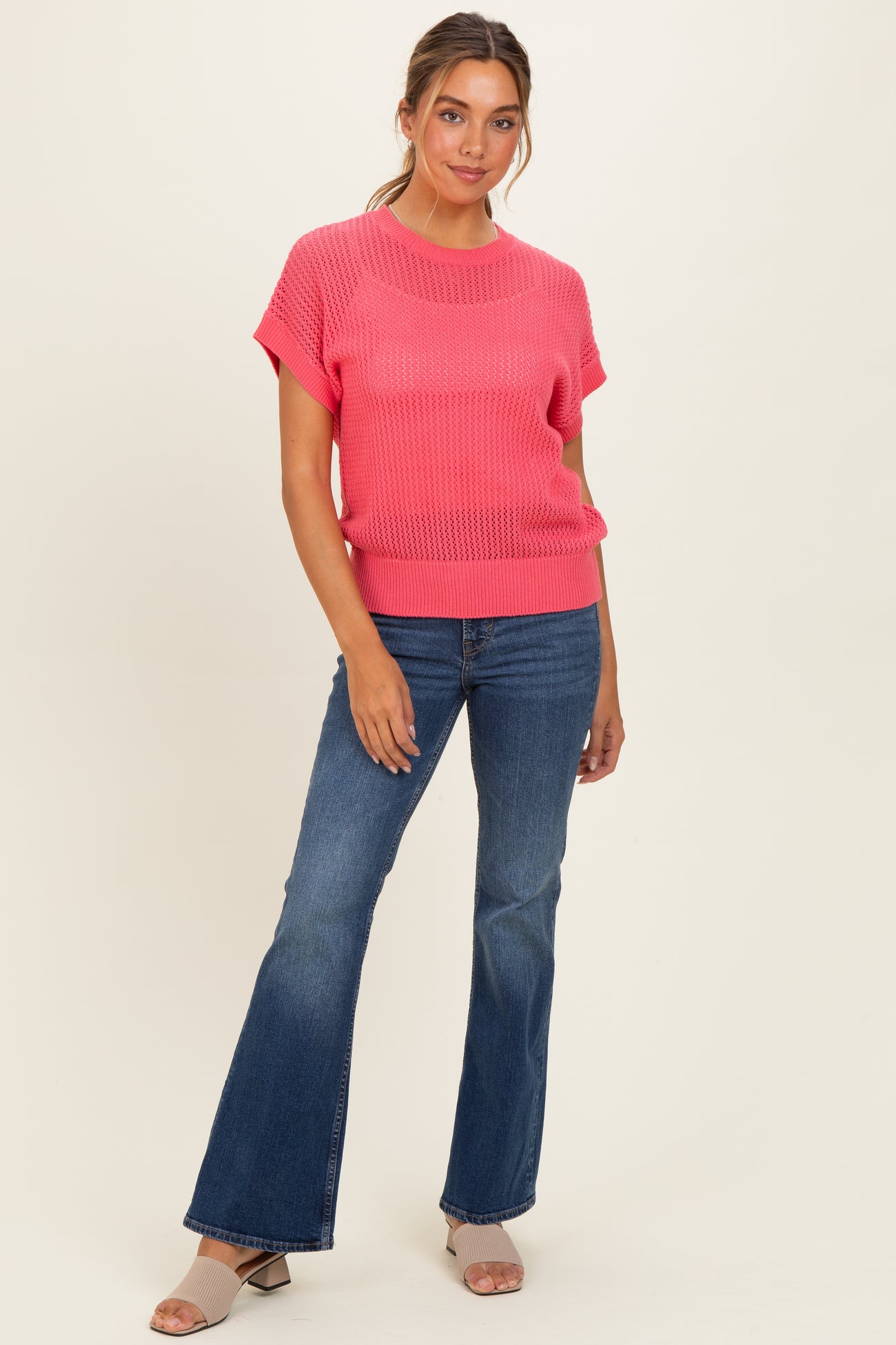 woman wearing a bright pink short sleeve sweater paired with flared blue jeans and heeled sandals