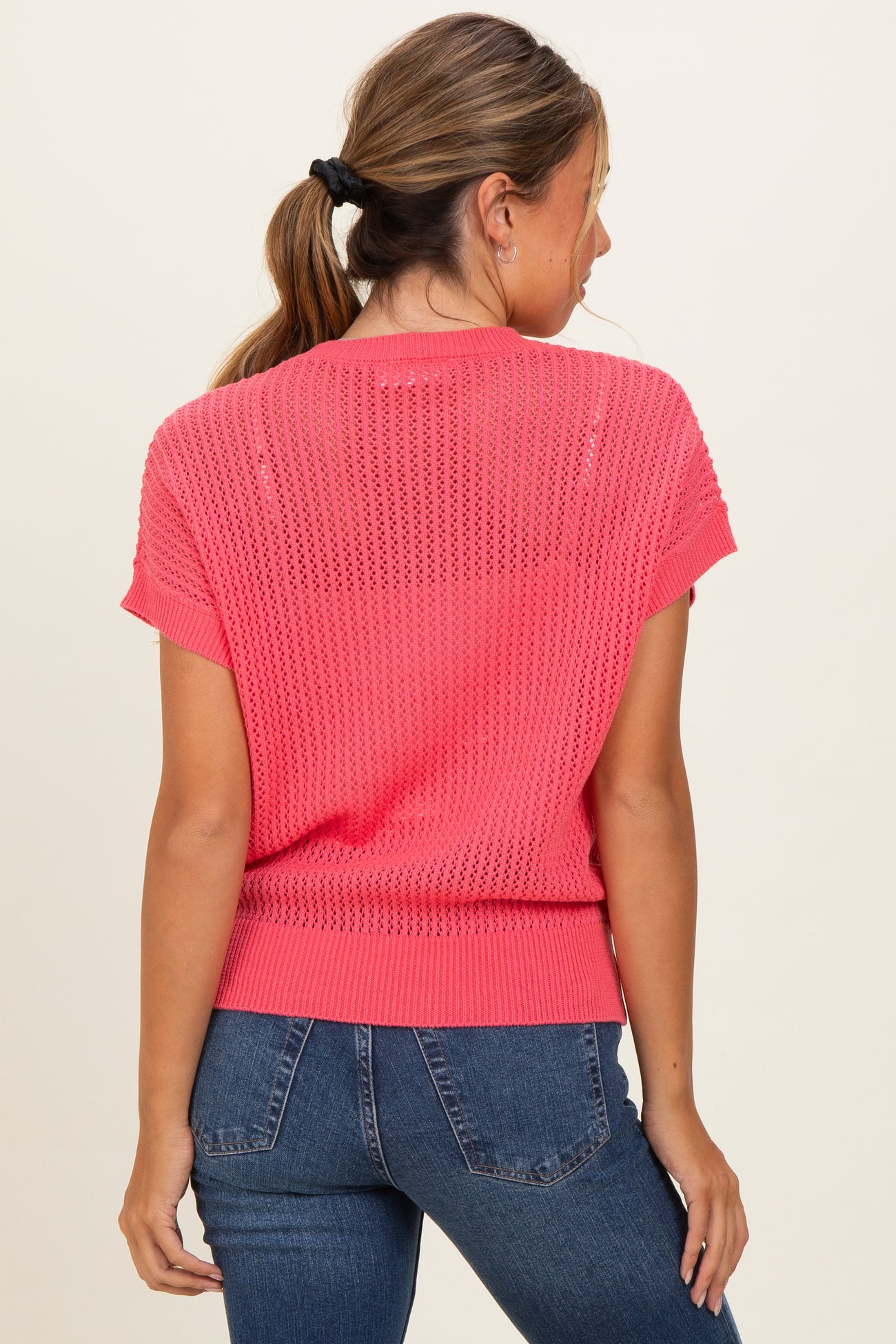 woman wearing a pink short sleeve knitted sweater with a loose fit and a rounded neckline, paired with jeans