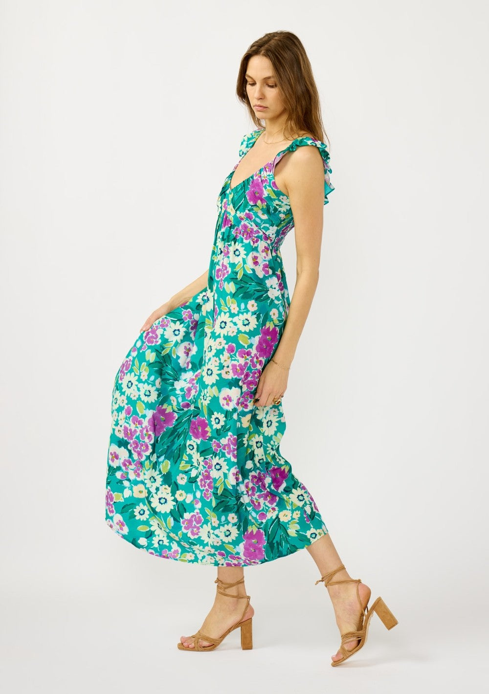 woman wearing a vibrant floral maxi dress with ruffled straps and a fitted bodice, styled with strappy sandals