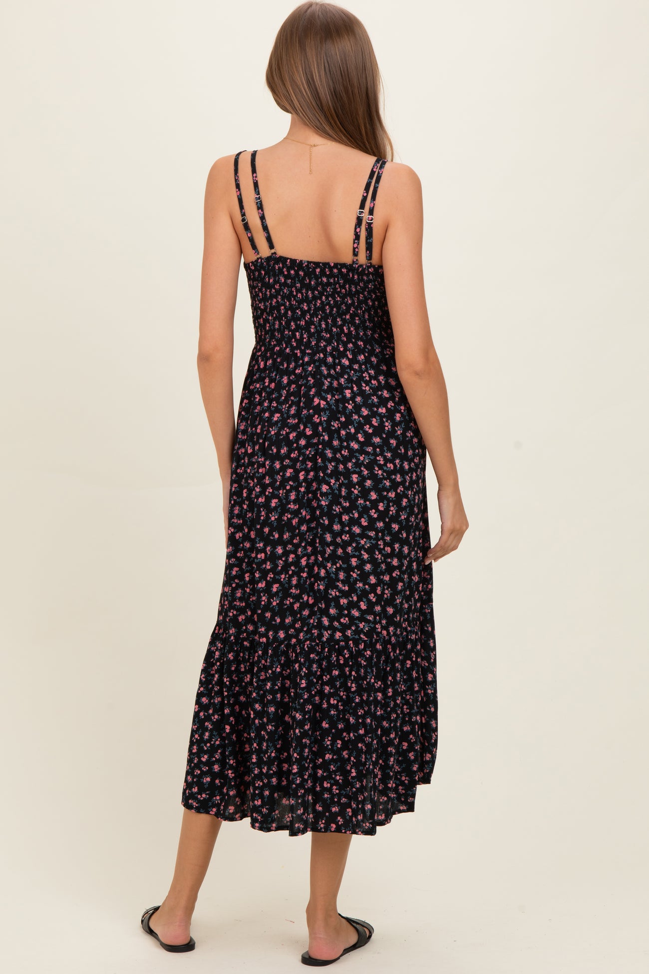 woman wearing a black floral maternity maxi dress with a smocked bodice and tiered ruffle hem, showing her back