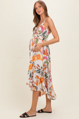 woman wearing a floral print maternity dress with a tiered skirt and adjustable straps, holding her baby bump