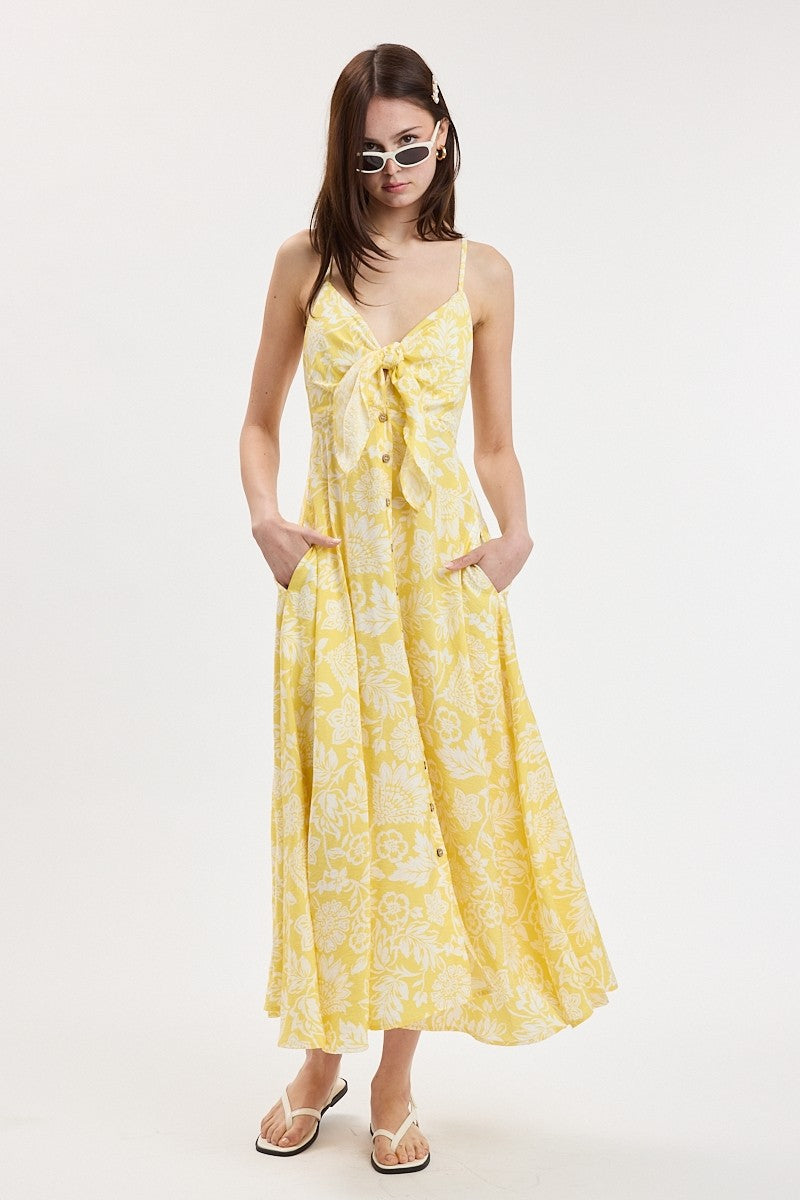 woman wearing a yellow floral maxi dress with adjustable straps and a bow detail at the waist