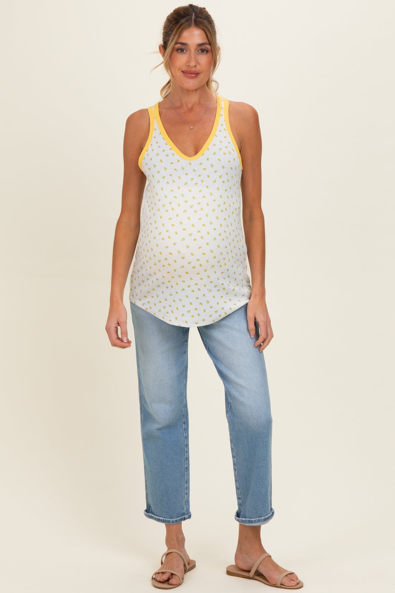 woman wearing a white maternity tank top with yellow polka dots and yellow trim, paired with light blue jeans and sandals, baby bump visible