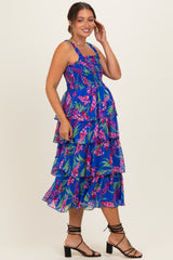 woman wearing a vibrant blue floral maternity dress with tiered layers and a smocked bodice, showcasing her baby bump