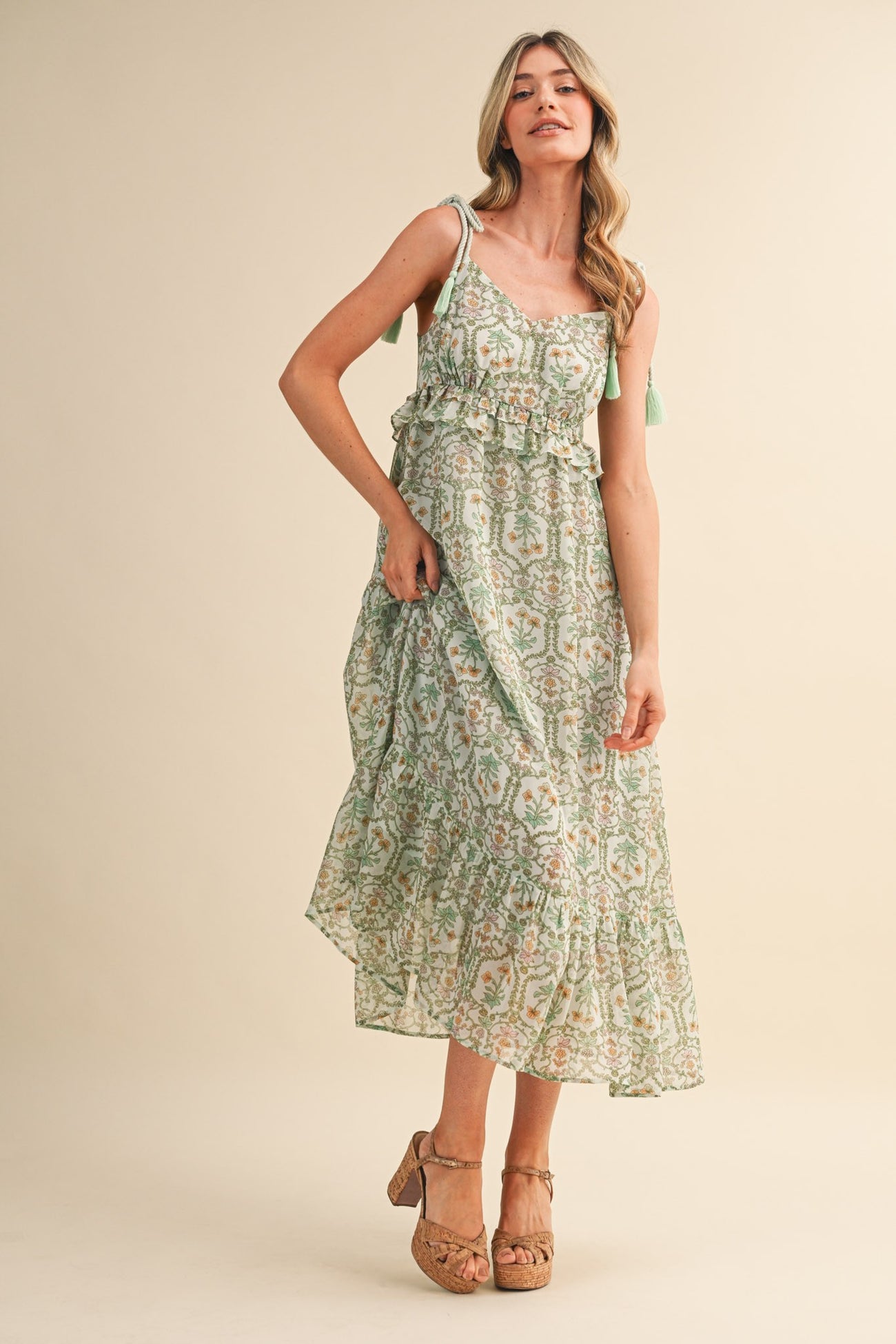 woman wearing a green and white floral maxi dress with adjustable straps and a ruffled hem