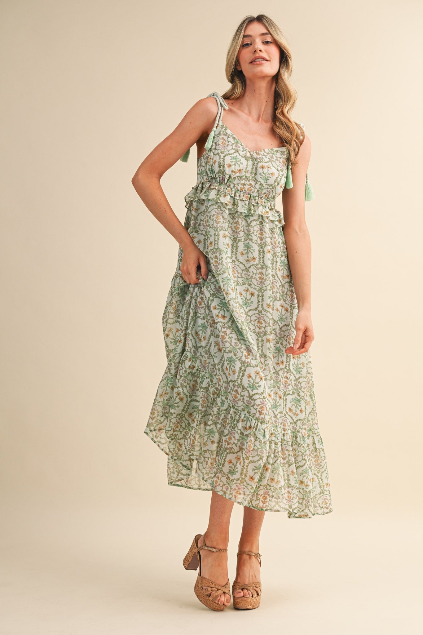 woman wearing a green and white floral maxi dress with adjustable straps and a ruffled hem
