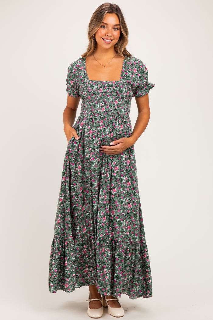 woman wearing a green floral maternity maxi dress with short puff sleeves and a square neckline, holding her baby bump