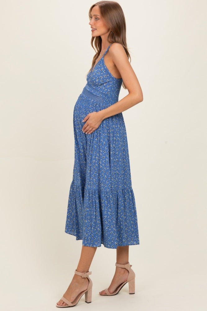 woman wearing a blue floral maternity dress, cradling her baby bump, standing in profile