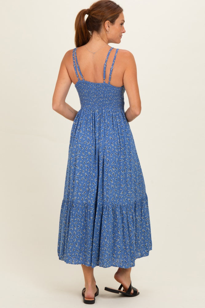 woman wearing a blue floral maxi dress with shoulder straps and a tiered skirt, seen from the back