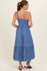 woman wearing a blue floral maxi dress with shoulder straps and a tiered skirt, seen from the back
