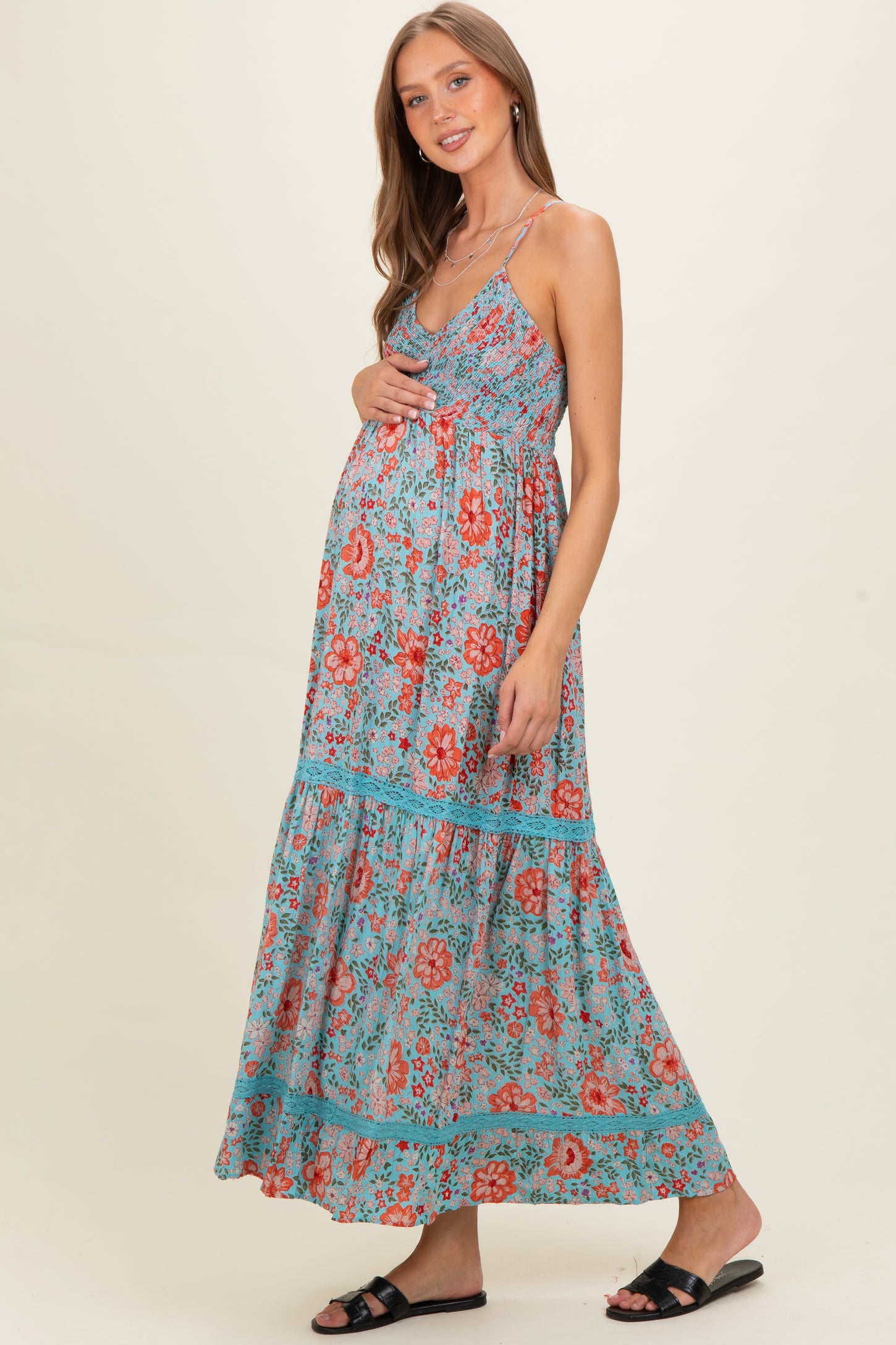 woman wearing a teal floral maxi dress, showing her baby bump, with a tiered skirt and spaghetti straps in maternity wear