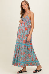 woman wearing a teal floral maxi dress, showing her baby bump, with a tiered skirt and spaghetti straps in maternity wear