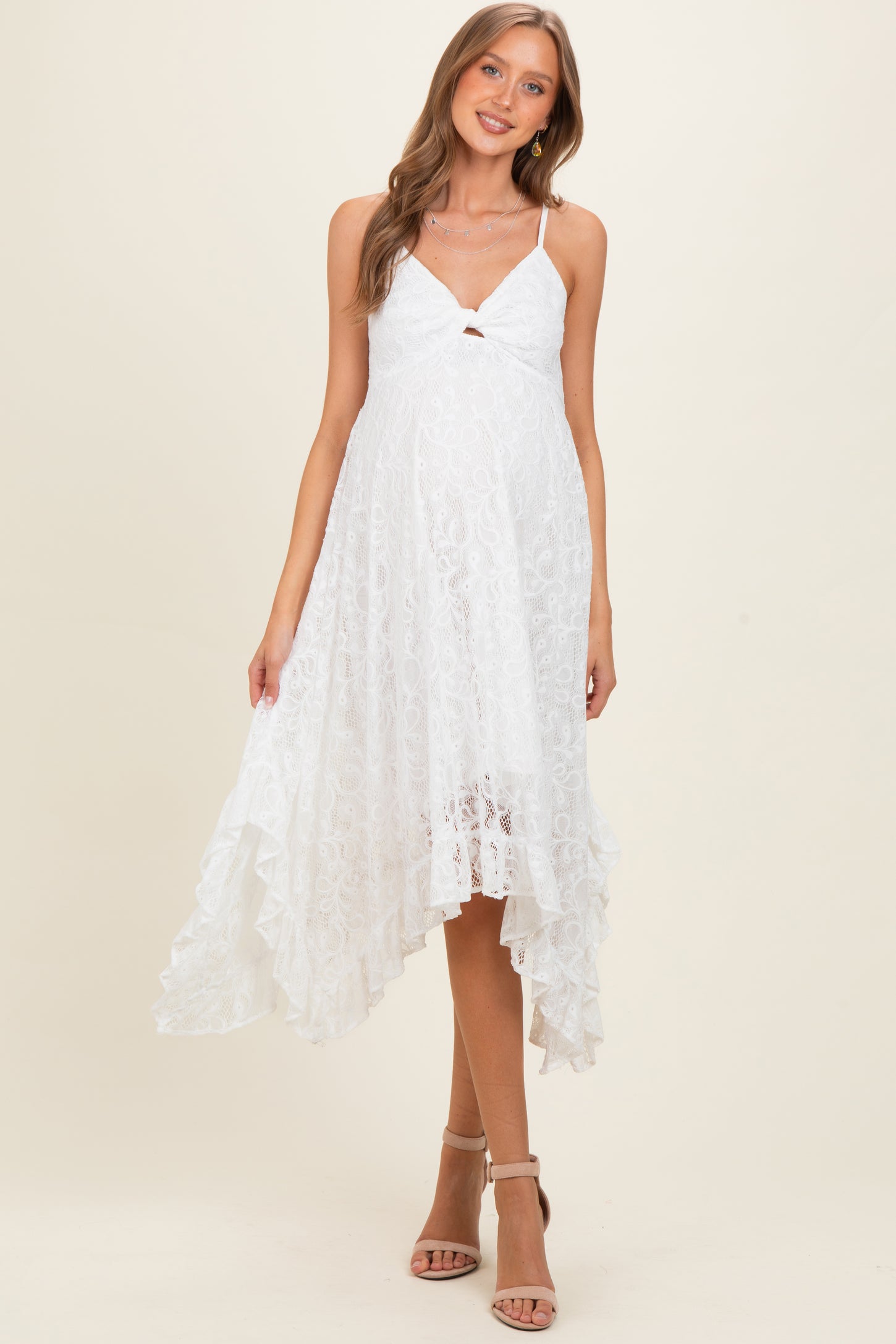 woman wearing a white lace maternity dress with a high-low hem and a tie detail at the bust, showcasing her baby bump