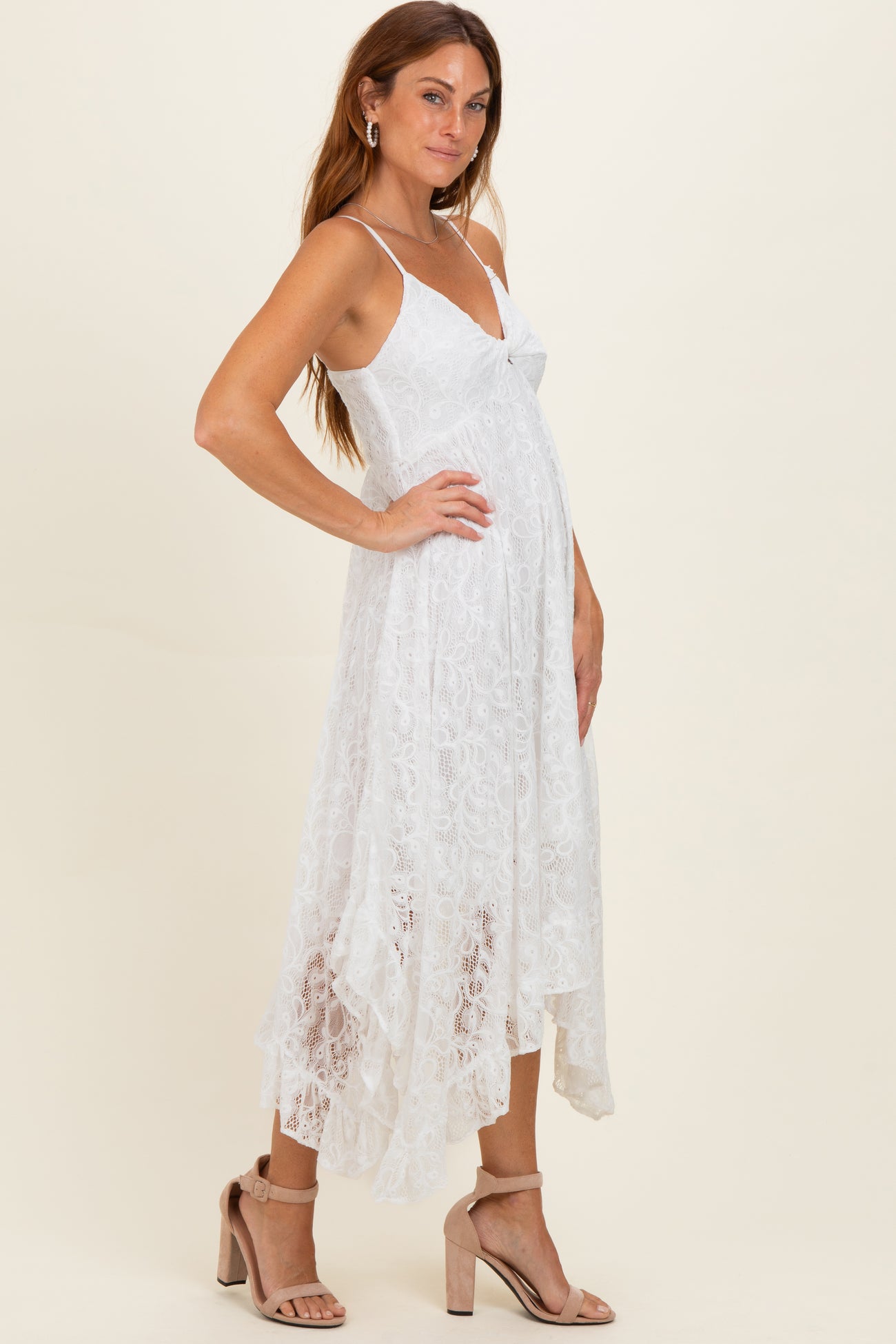woman wearing a white lace midi dress with a high-low hem and spaghetti straps paired with nude heeled sandals