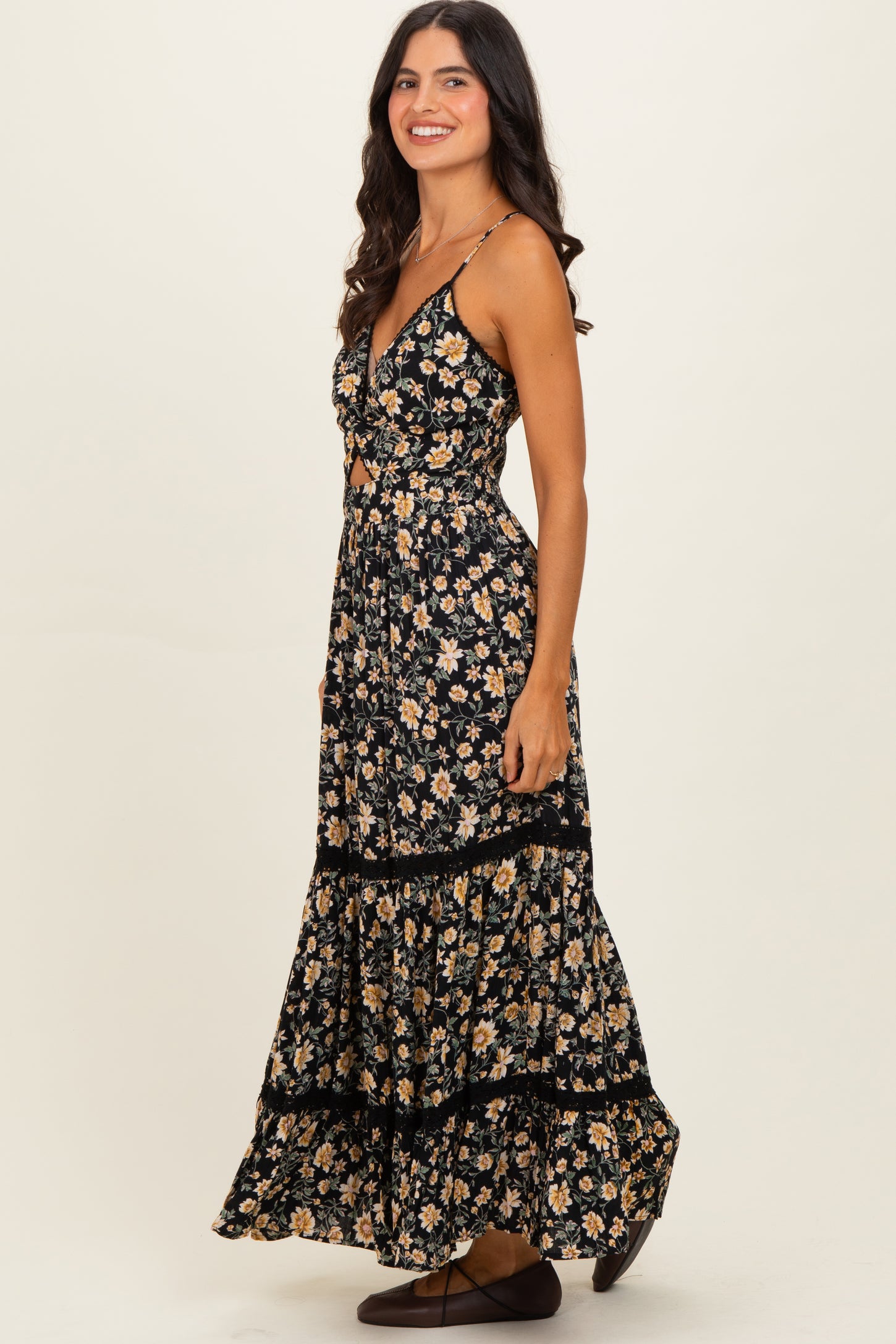 woman wearing a black floral maxi dress with a fitted top and tiered skirt, standing in profile