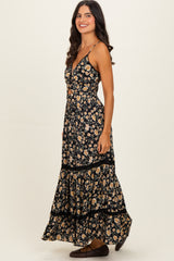woman wearing a black floral maxi dress with a fitted top and tiered skirt, standing in profile