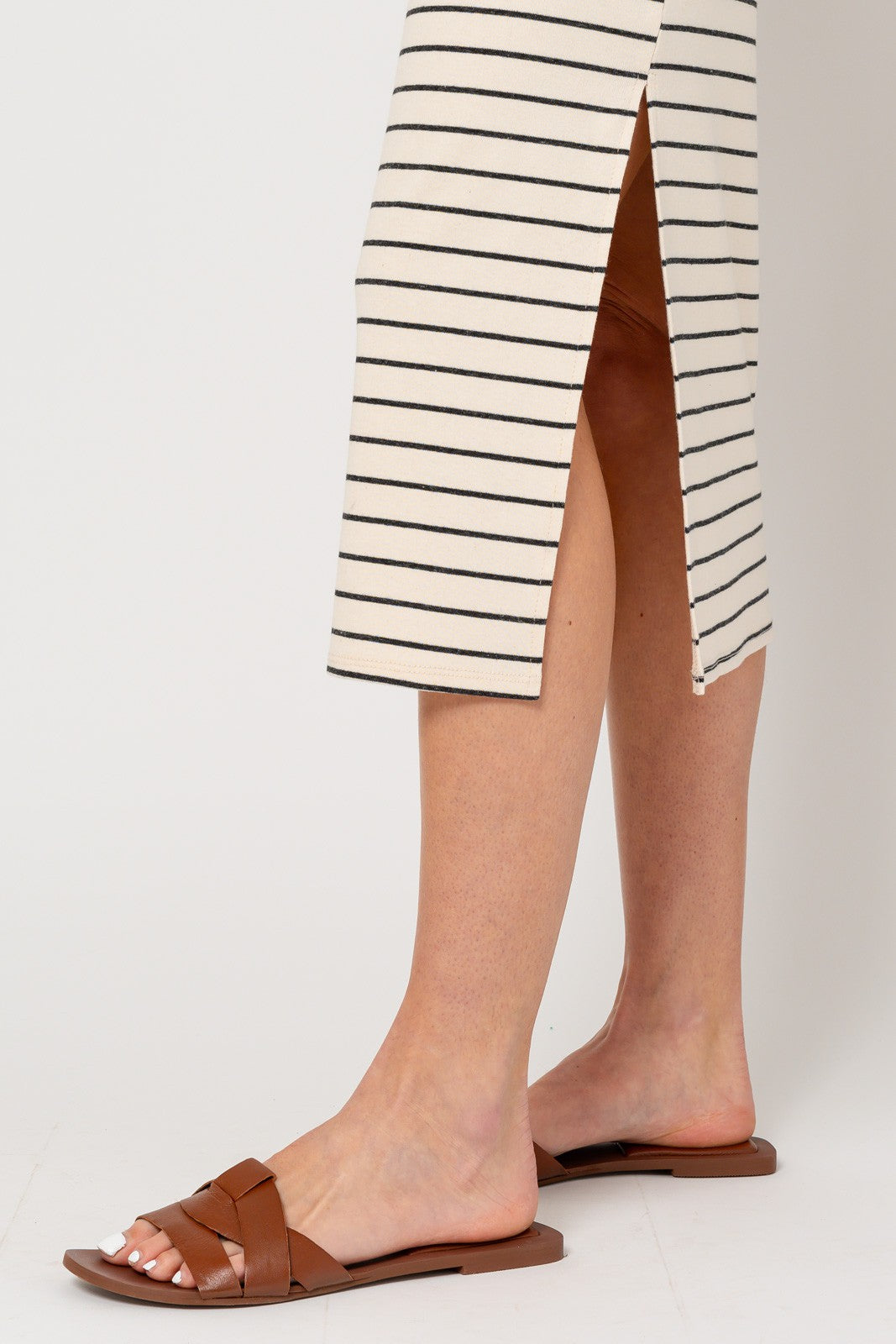 woman wearing brown flat slide sandals with a woven detail, paired with a striped midi dress featuring side slits
