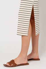 woman wearing brown flat slide sandals with a woven detail, paired with a striped midi dress featuring side slits