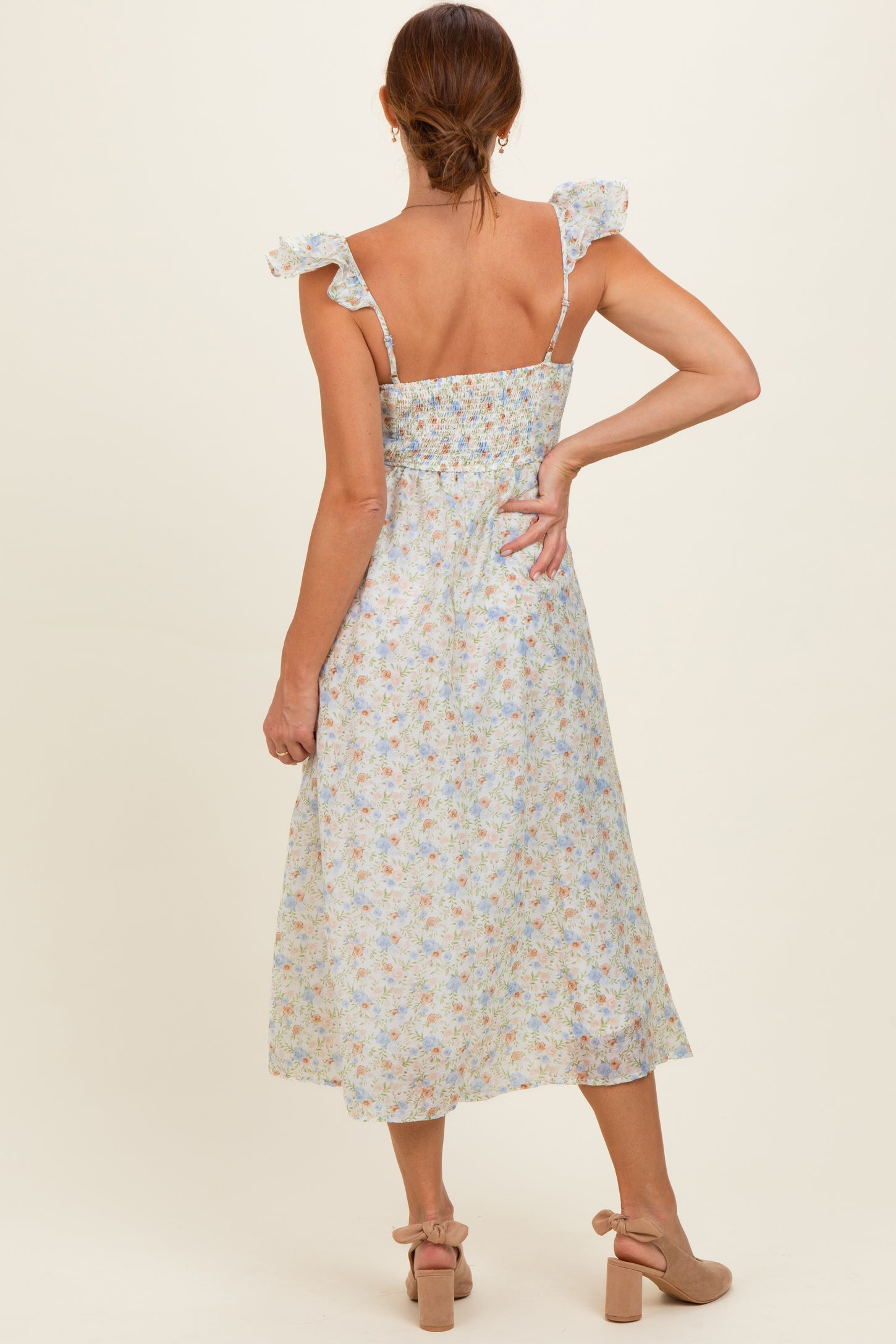 woman wearing a light floral midi dress with ruffled shoulder straps, showing the back and a fitted smocked bodice