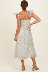 woman wearing a light floral midi dress with ruffled shoulder straps, showing the back and a fitted smocked bodice