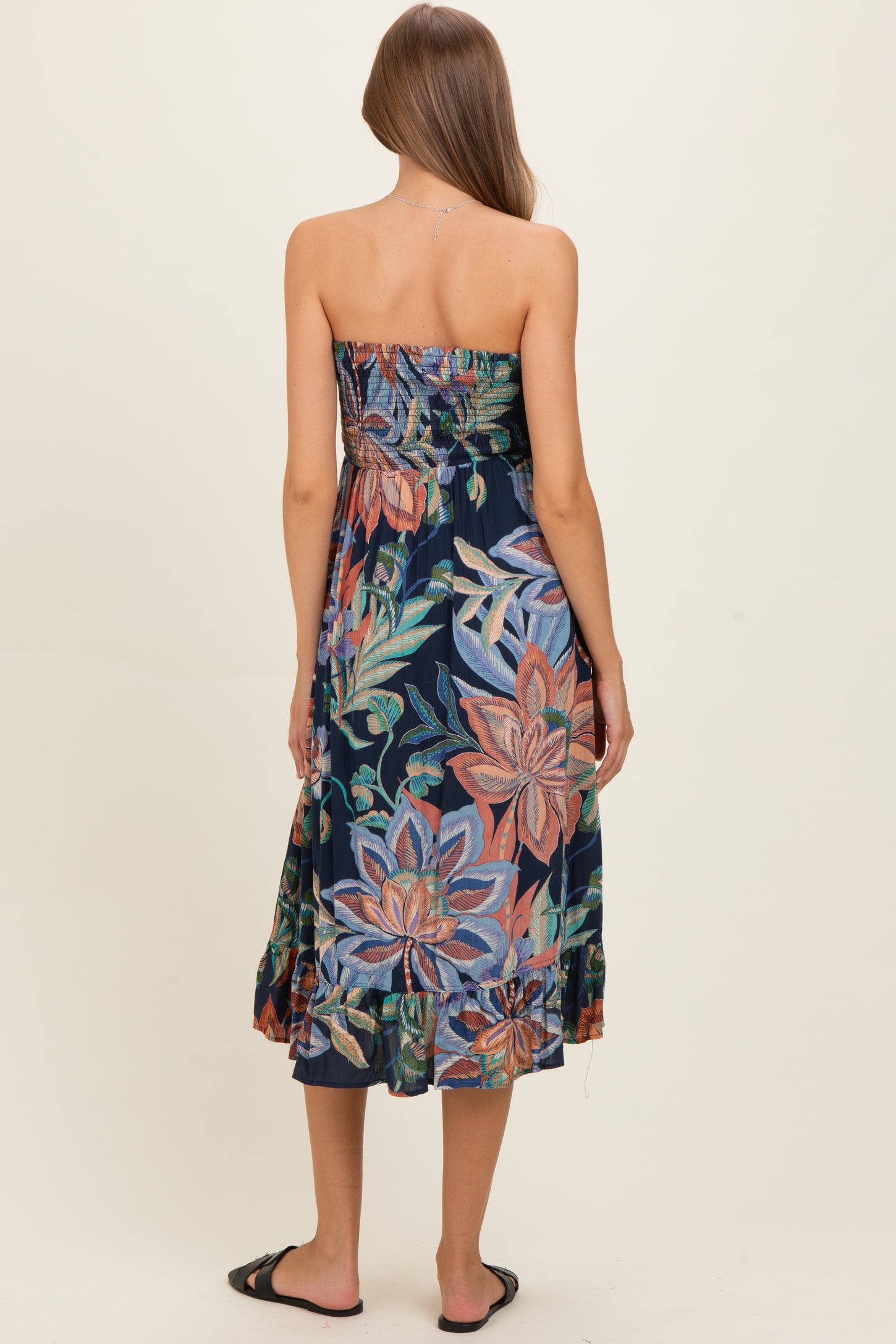 woman wearing a colorful floral strapless maternity dress with a tiered hem, showing her baby bump from the back.