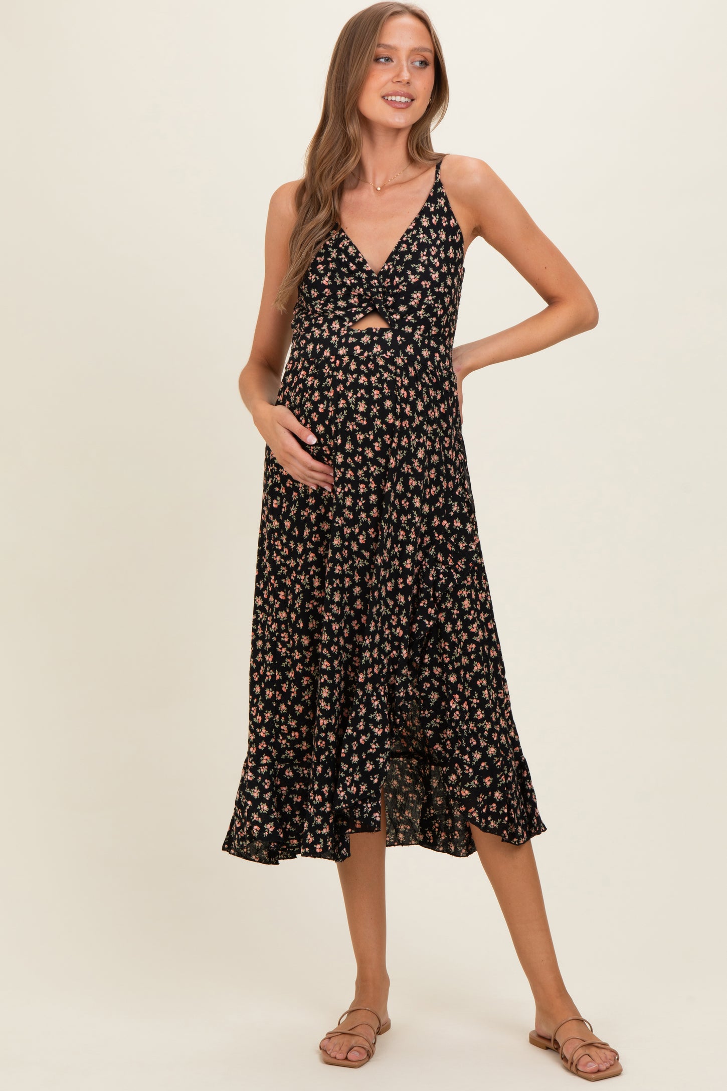 woman wearing a black floral maternity dress with a knot front detail and a flowy hem, highlighting her baby bump