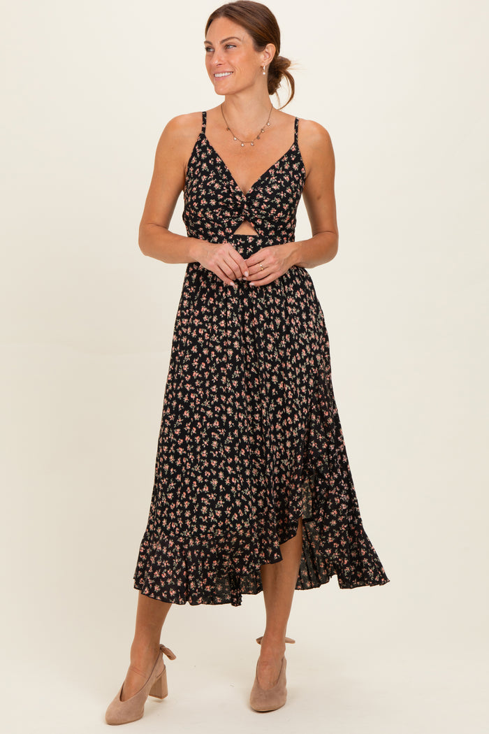 woman wearing a black floral midi dress with a front twist detail and spaghetti straps, paired with nude heels