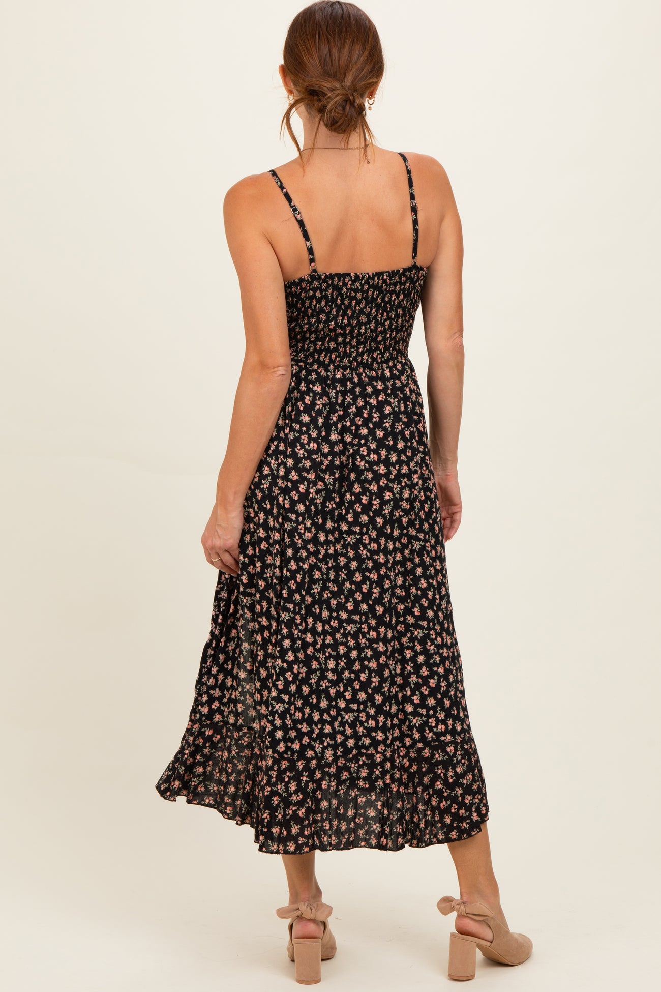 woman wearing a black floral midi dress with thin straps and a smocked bodice, standing with her back to the camera