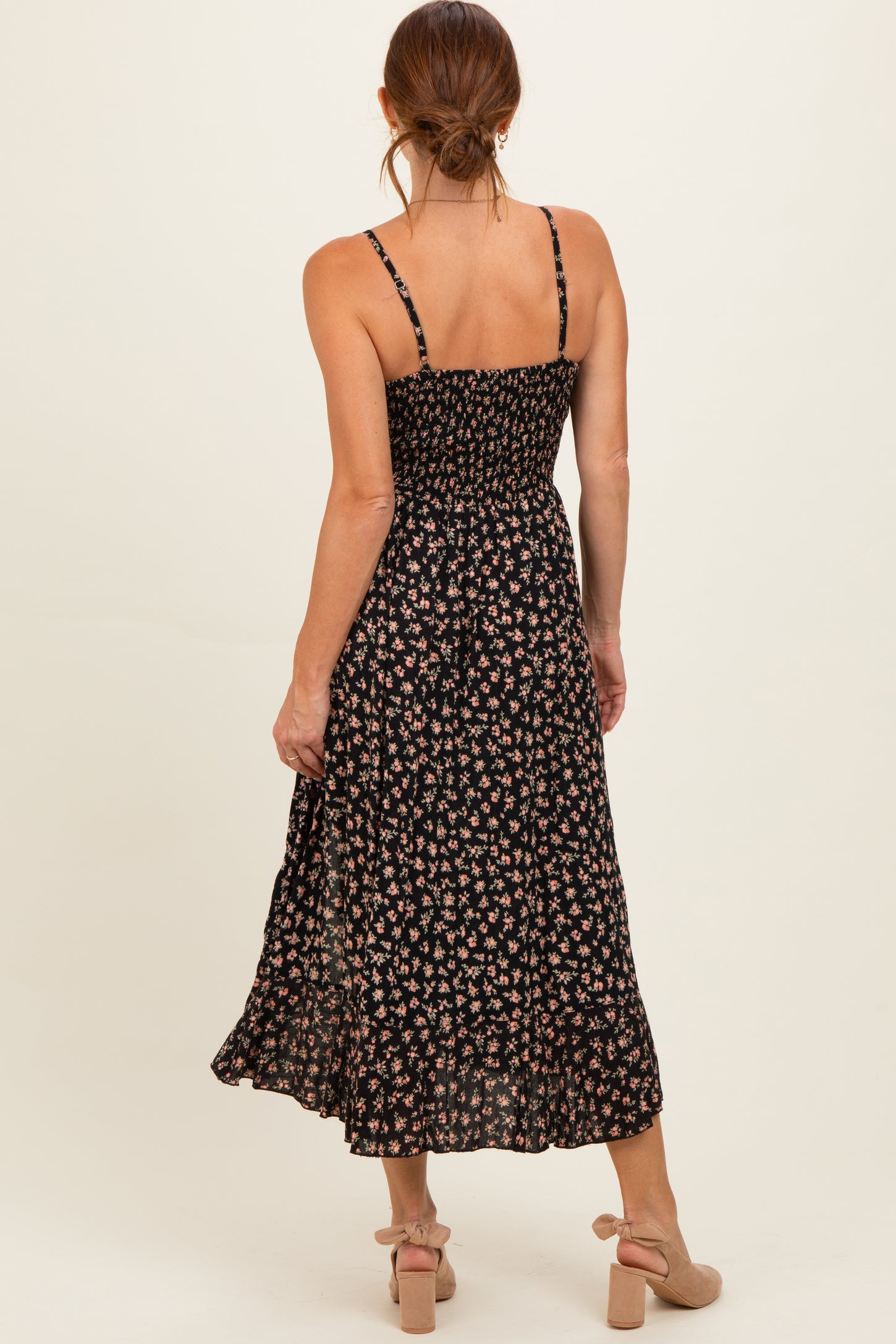 woman wearing a black floral midi dress with thin straps and a smocked bodice, standing with her back to the camera