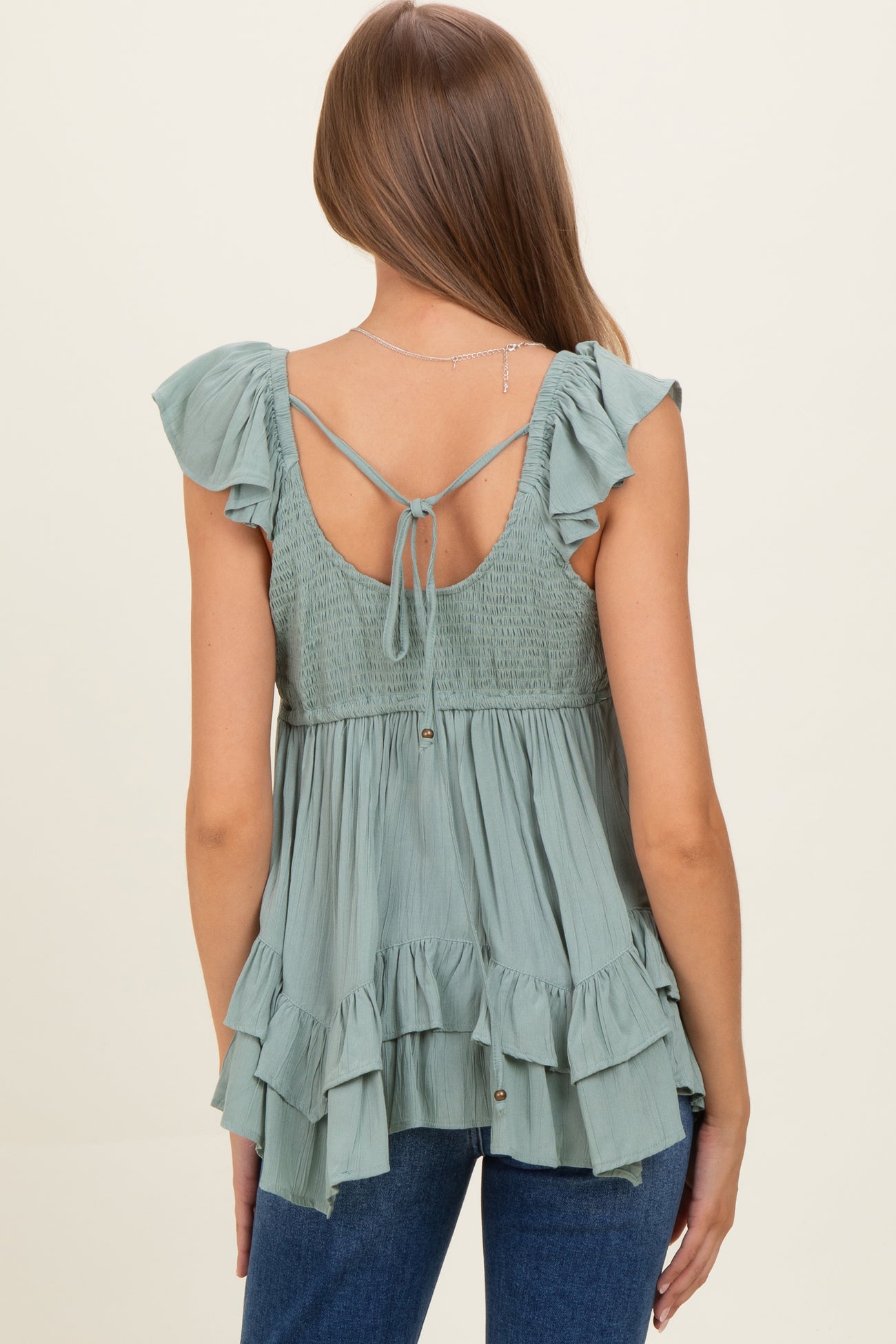woman wearing a sage green maternity top with ruffled sleeves and a smocked back detail, showing a loose fit