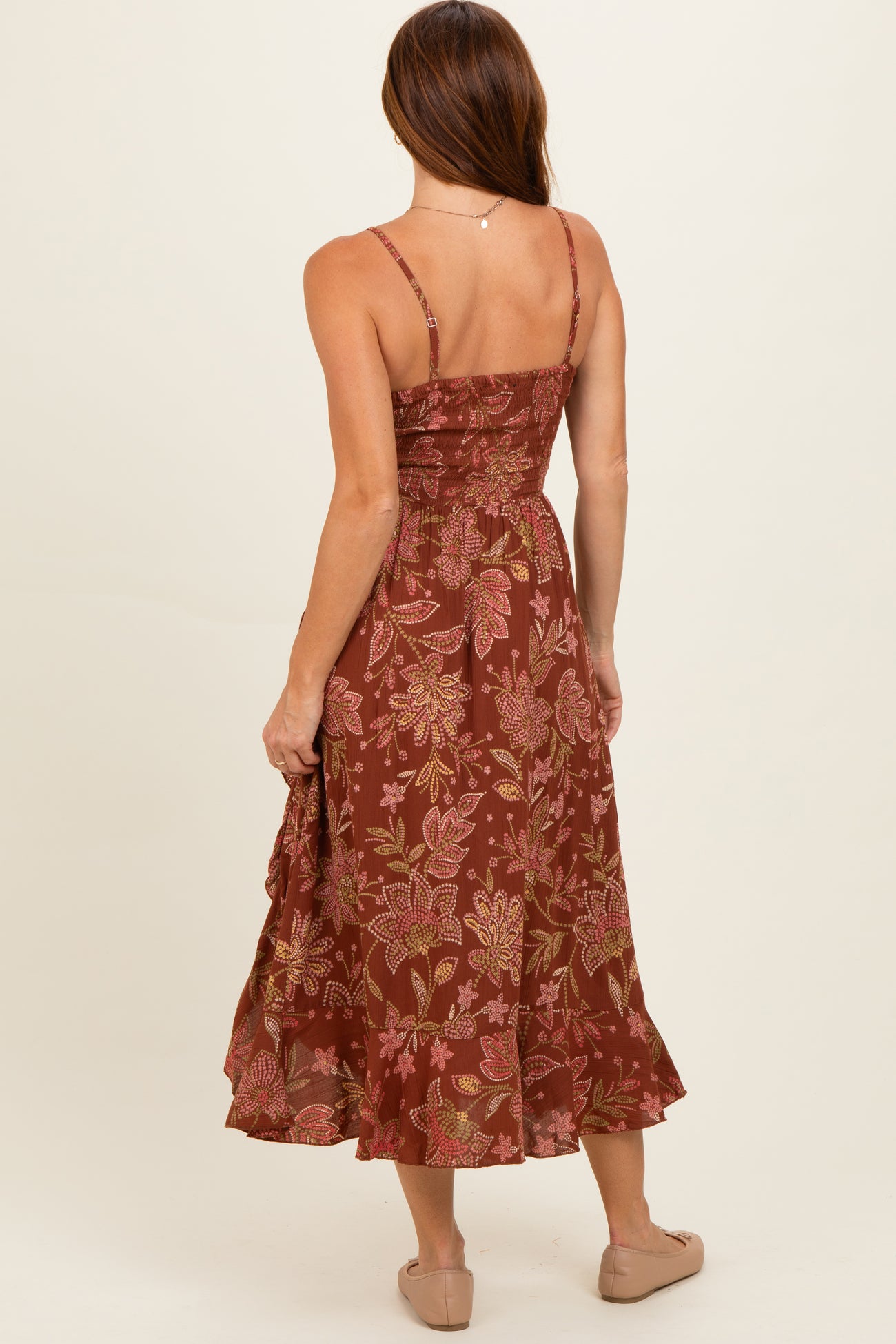 woman wearing a spaghetti strap brown floral midi dress, showing a fitted bodice and flowing skirt from the back