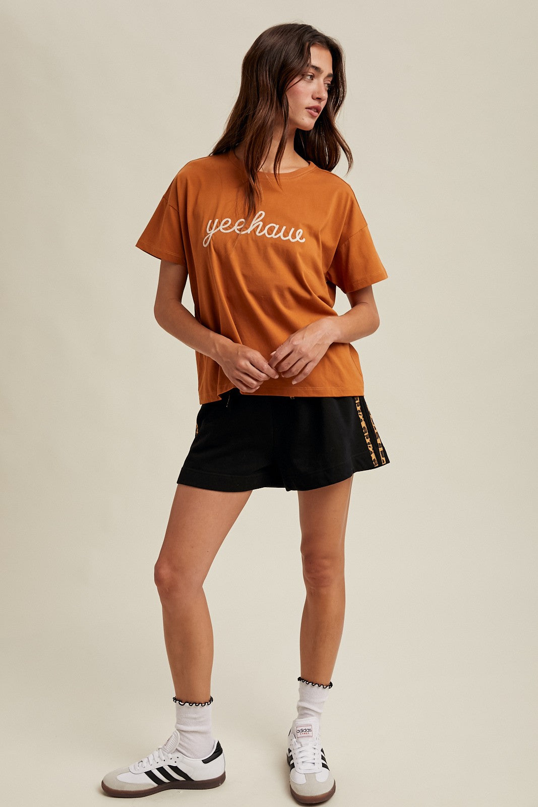 woman wearing an orange graphic tee with "yeehaw" text and black shorts, styled with athletic socks and sneakers