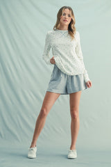 woman wearing a cream long sleeve pullover with floral pattern and gray drawstring shorts, styled with white sneakers