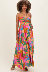 woman wearing a colorful floral maternity maxi dress with a twist front and adjustable straps, showcasing her baby bump