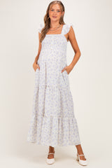 woman wearing a white floral maternity maxi dress with ruffle straps and pockets, showcasing her baby bump