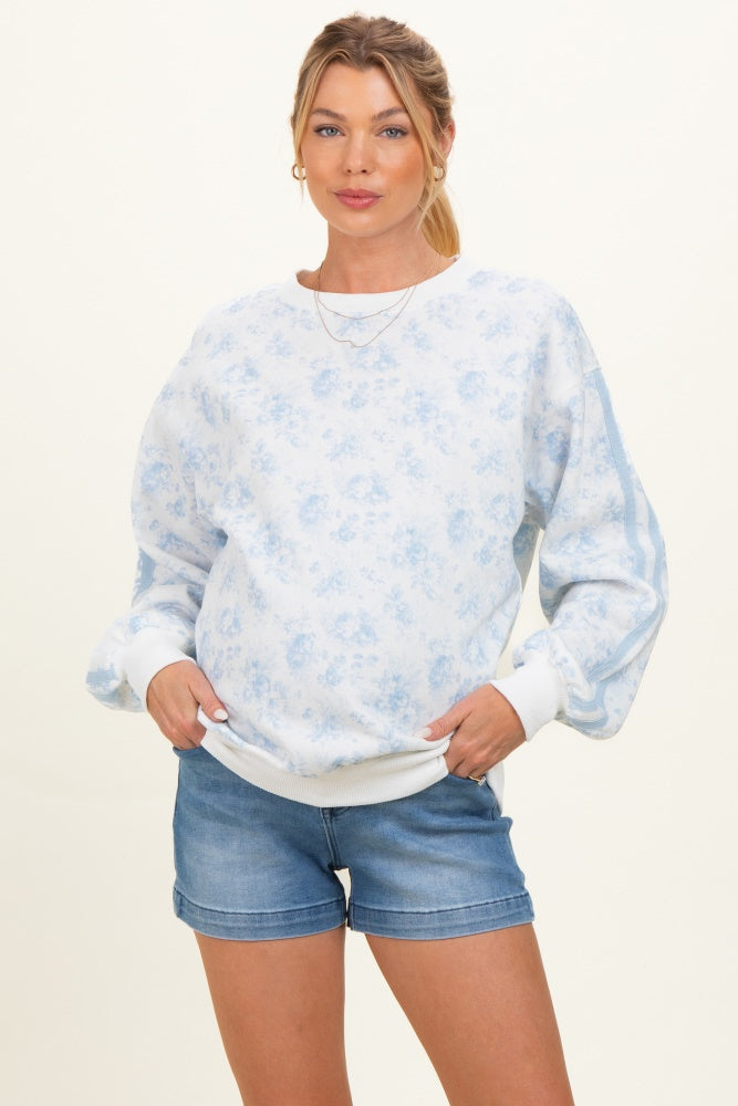 woman wearing a light blue floral patterned maternity sweatshirt with puff sleeves and denim shorts, showing her baby bump