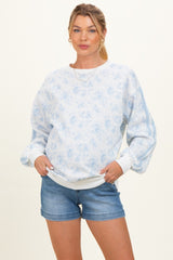 woman wearing a light blue floral patterned maternity sweatshirt with puff sleeves and denim shorts, showing her baby bump