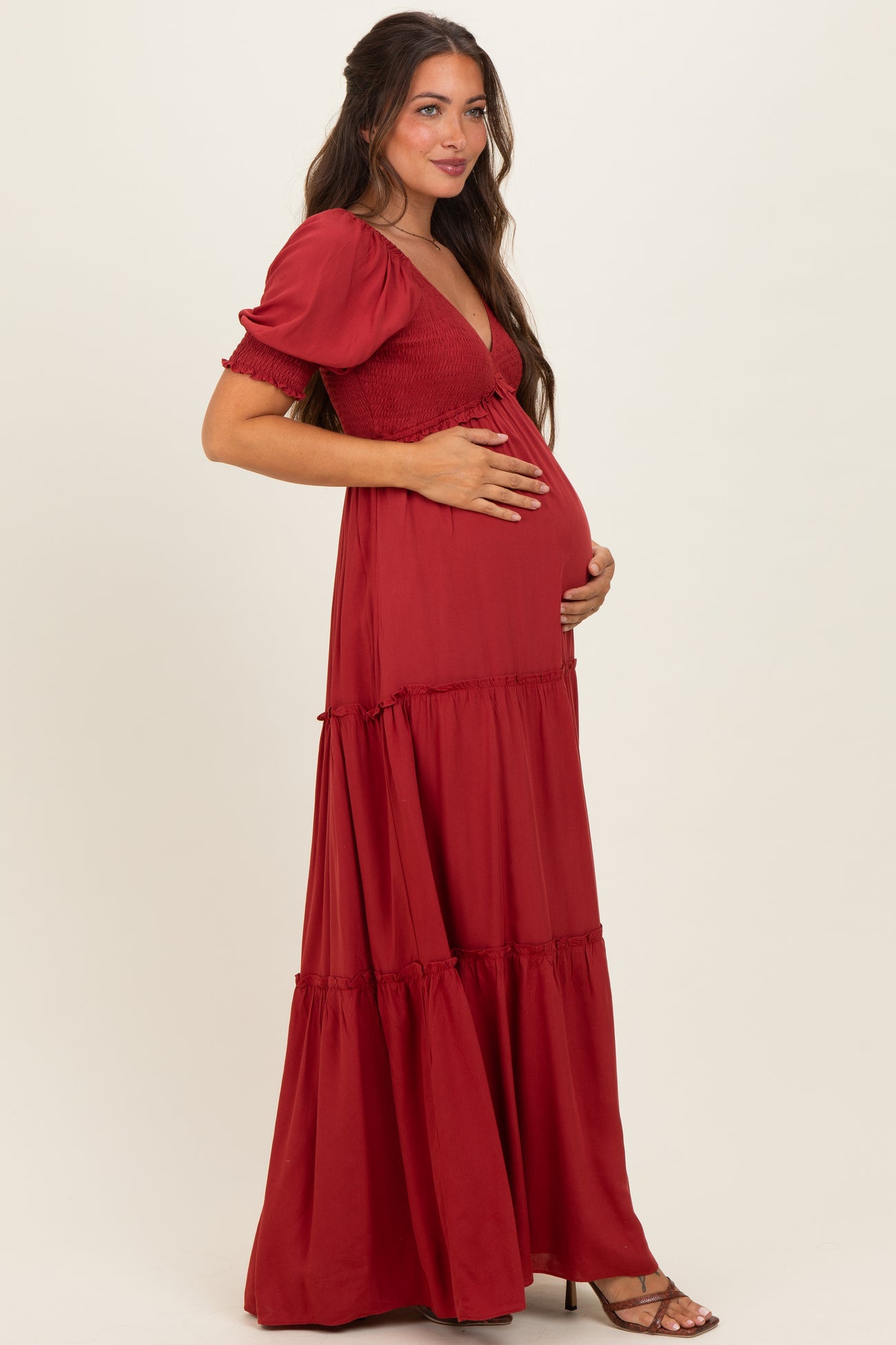 woman wearing a red maternity maxi dress with puff sleeves and smocked bodice, holding her baby bump