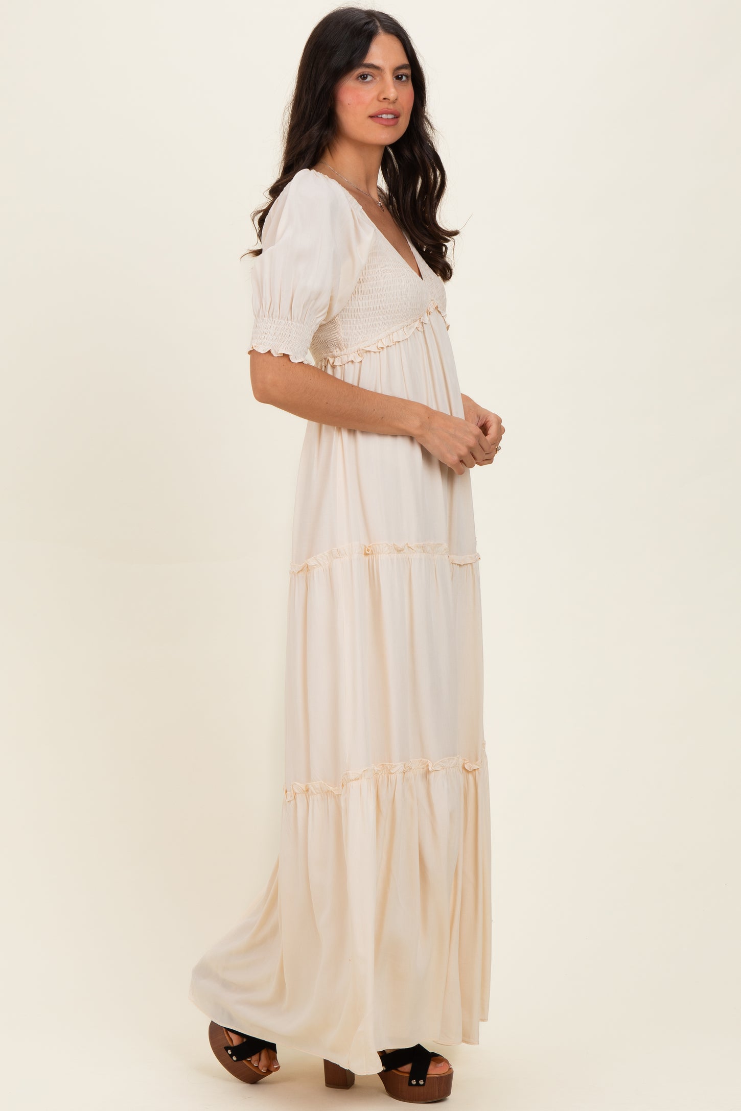 woman wearing a cream maxi dress with puffed sleeves and smocked bodice, standing sideways against a light backdrop