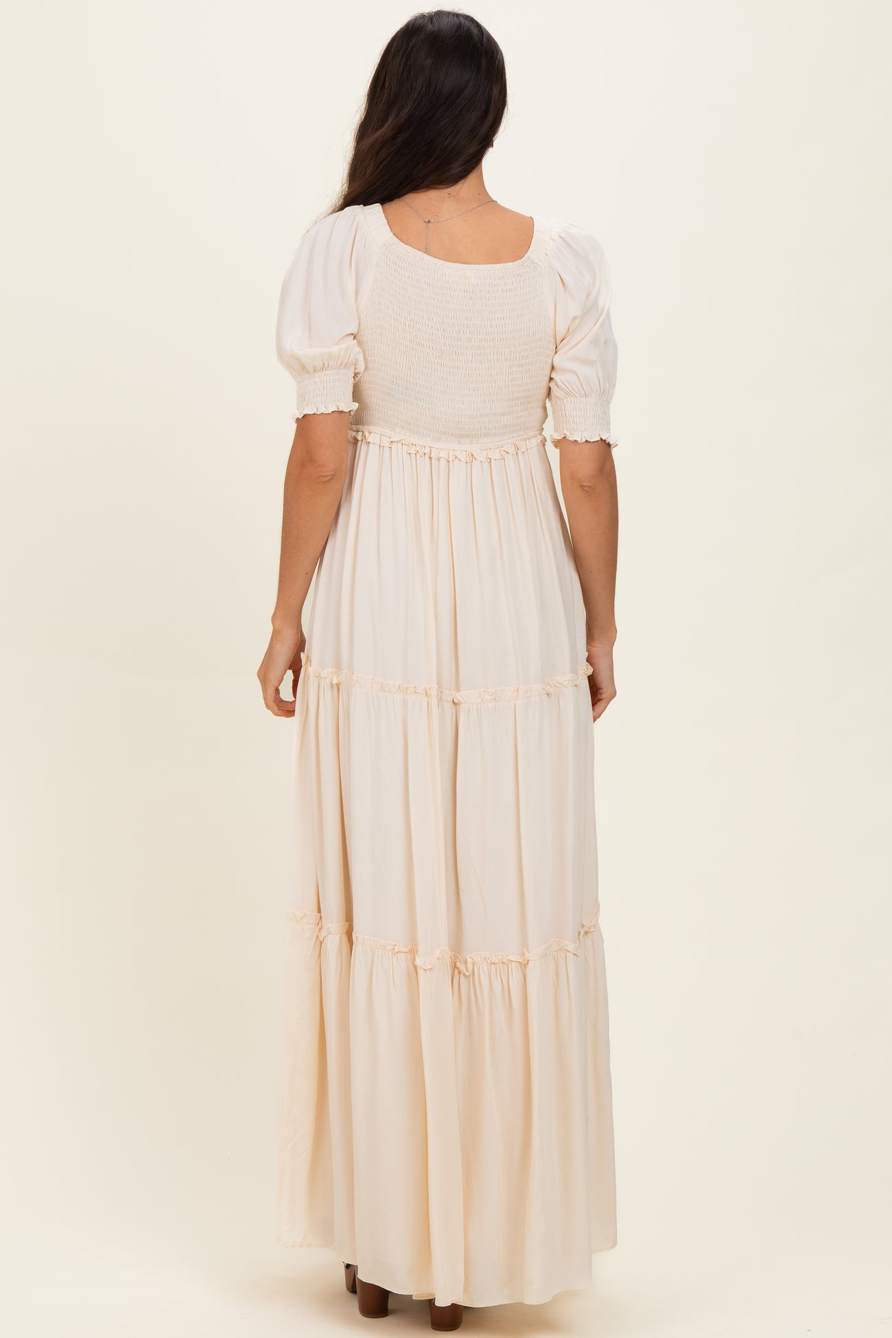 woman wearing a light beige maxi dress with puff sleeves and a smocked bodice, viewed from the back