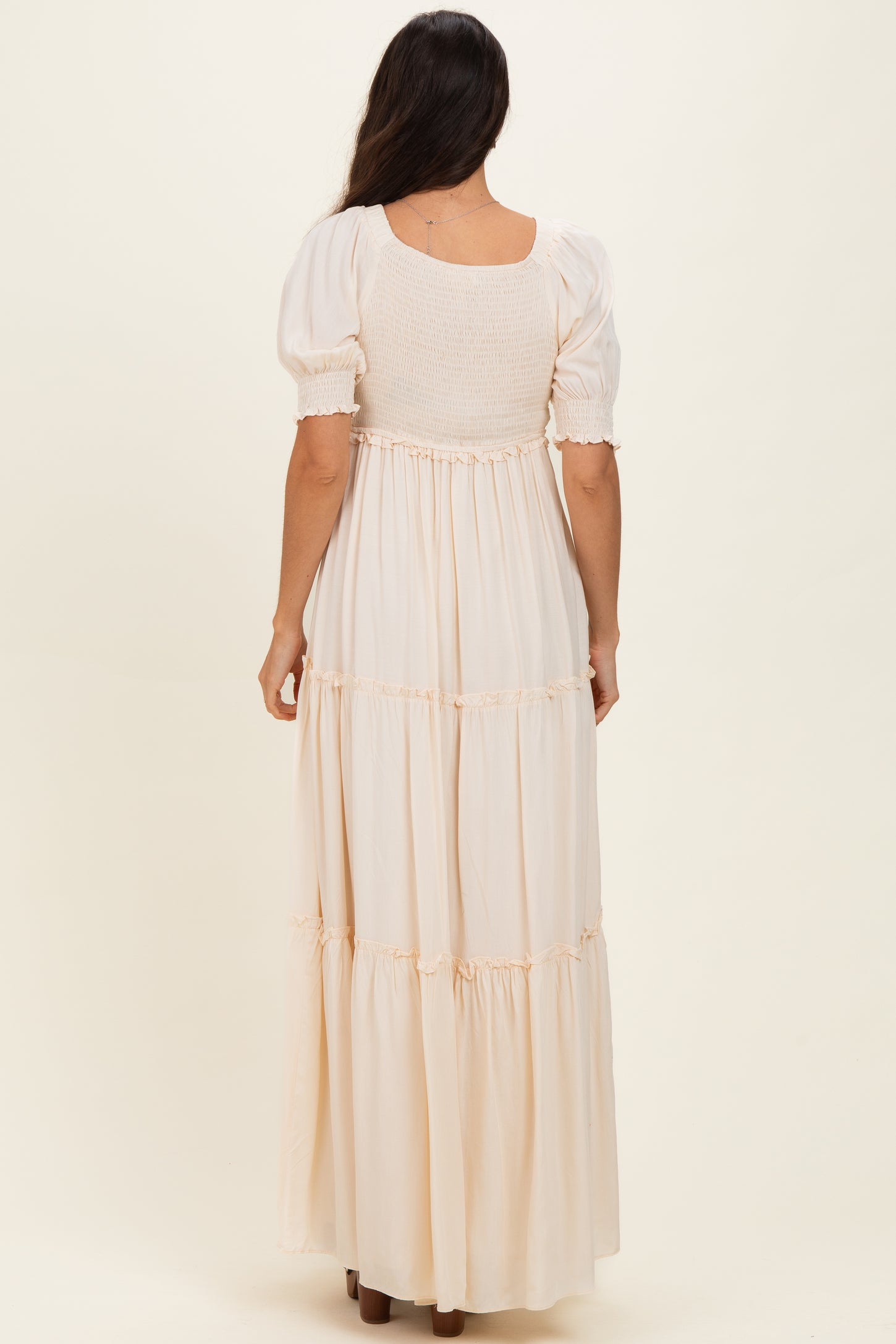 woman wearing a light beige maxi dress with puff sleeves and a smocked bodice, viewed from the back