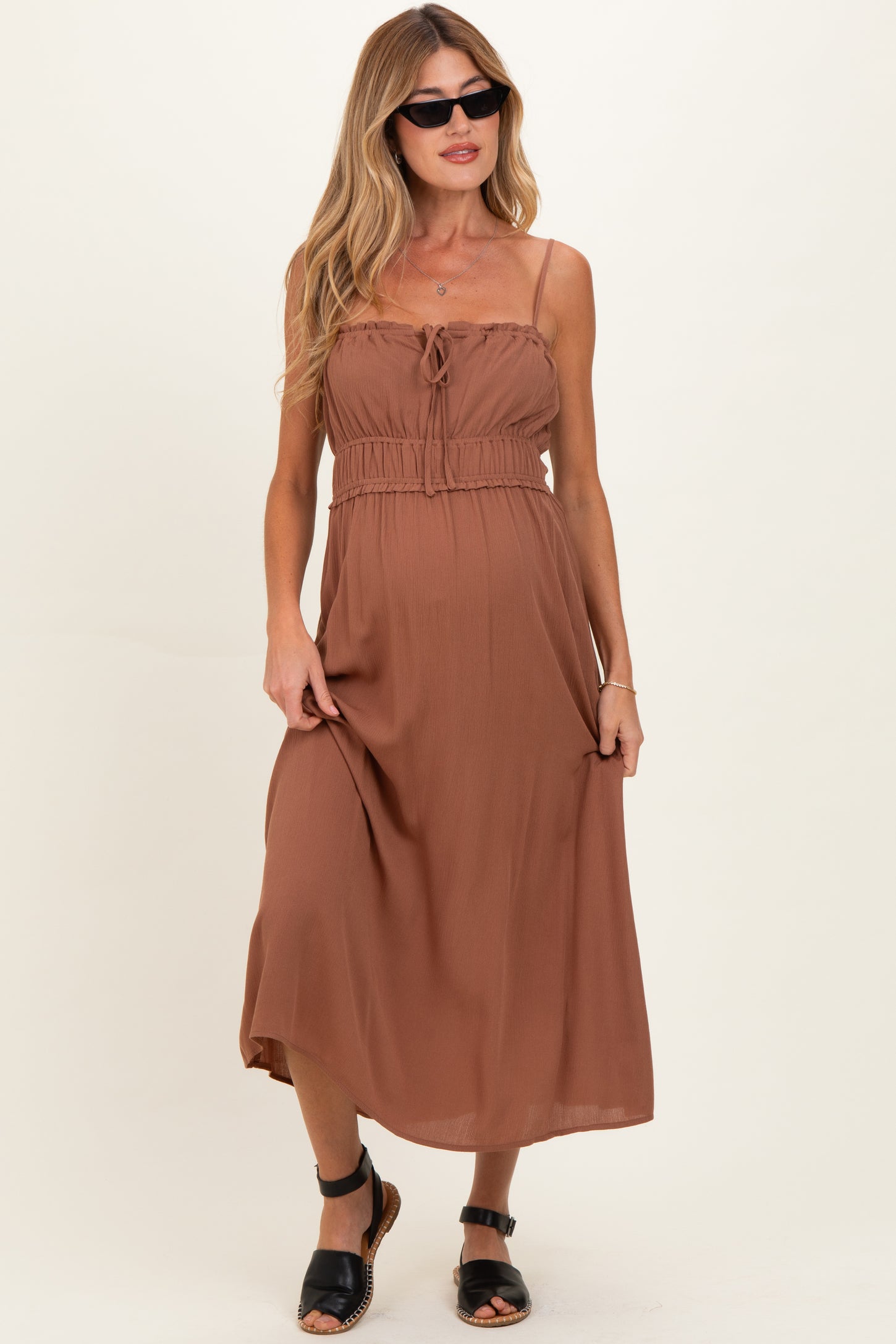 woman wearing a brown maternity maxi dress with spaghetti straps and an adjustable waist, styled with sunglasses