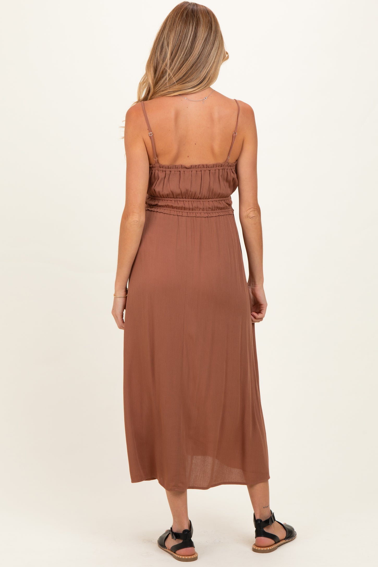 woman wearing a rust-colored maternity maxi dress with adjustable straps and an elastic waistband, seen from the back