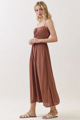 woman wearing a brown maxi dress with a smocked bodice and adjustable straps, paired with slip-on sandals