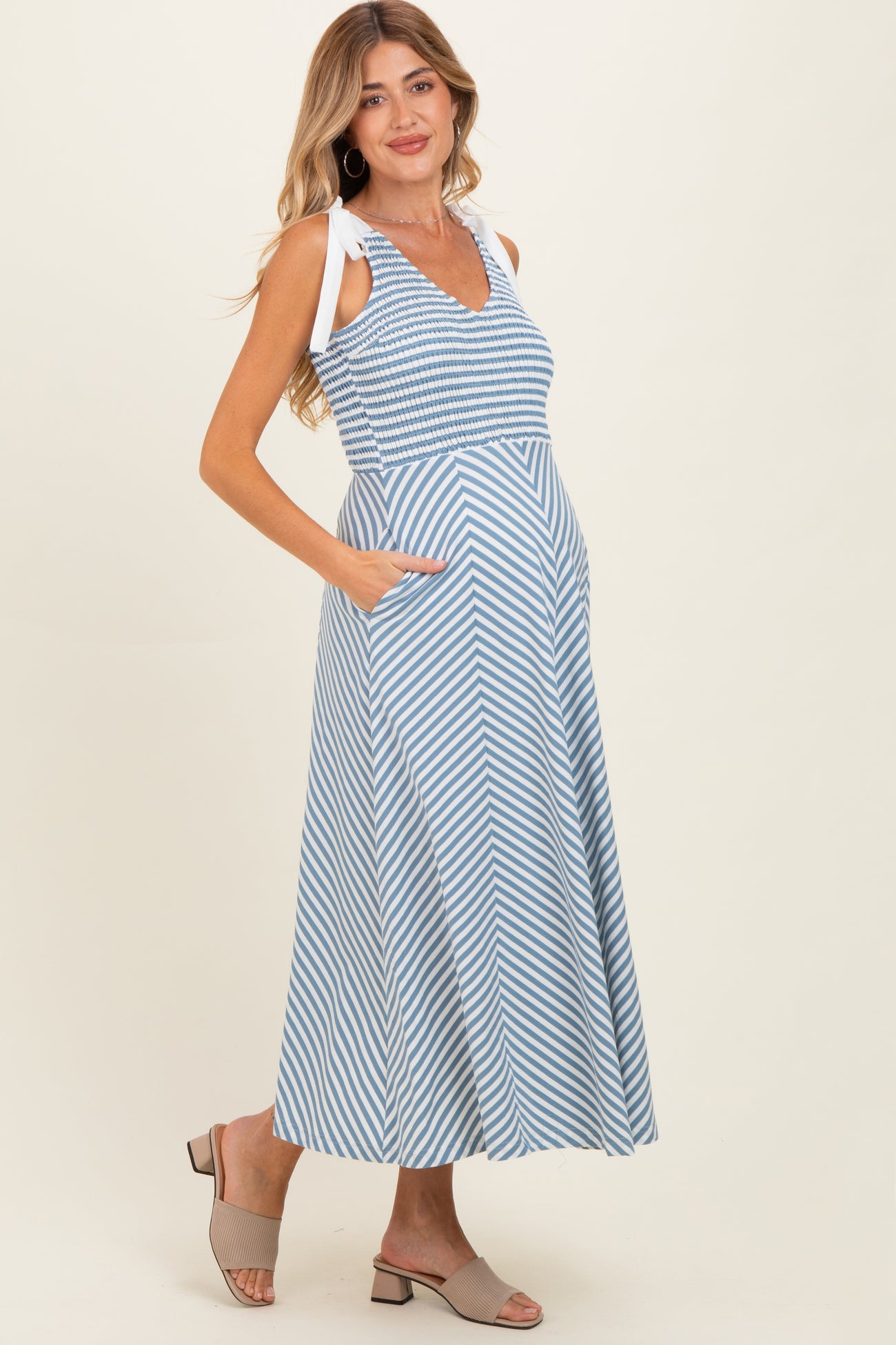 woman wearing a blue and white striped maternity maxi dress with side pockets and adjustable straps, showcasing her baby bump