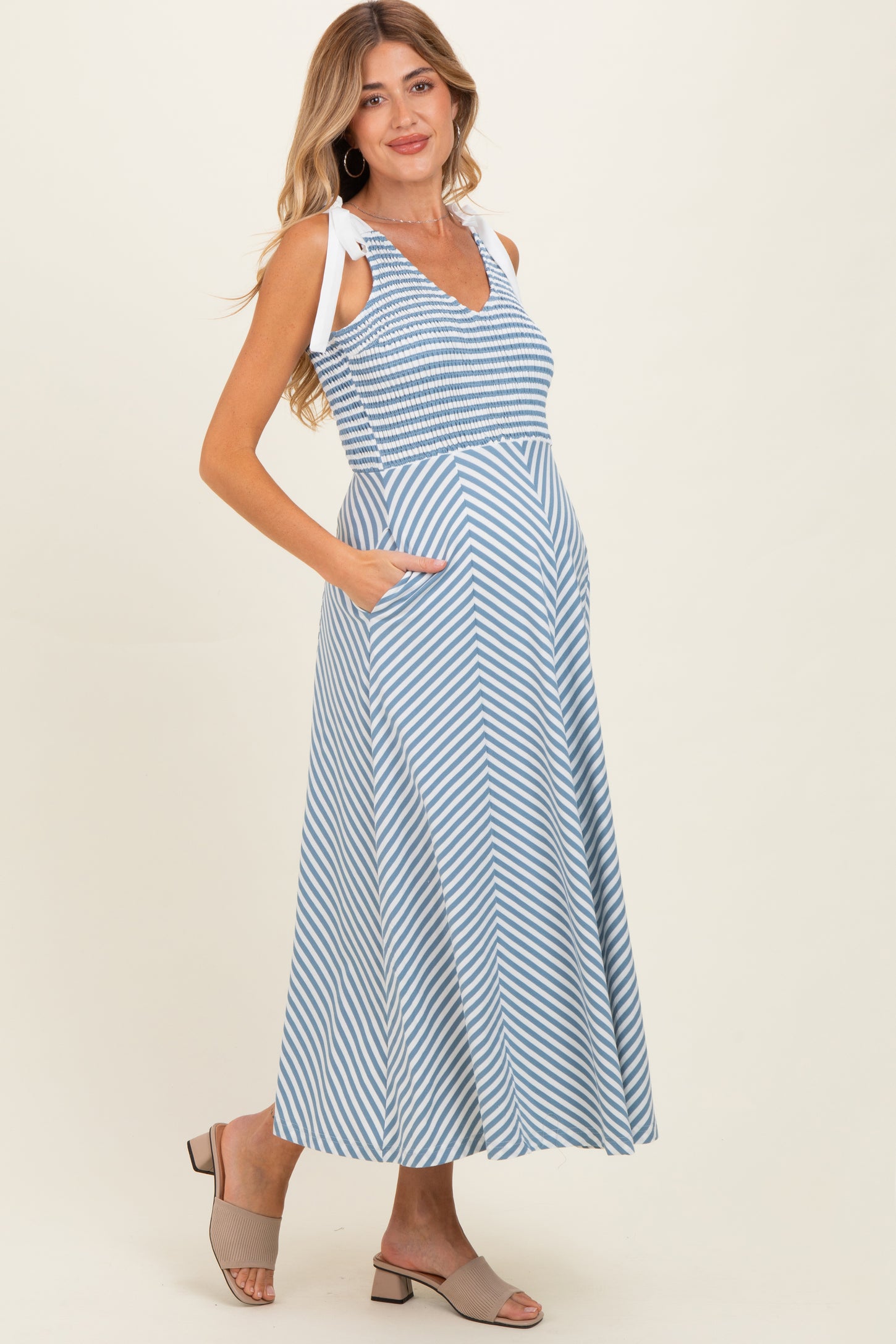 woman wearing a blue and white striped maternity maxi dress with side pockets and adjustable straps, showcasing her baby bump