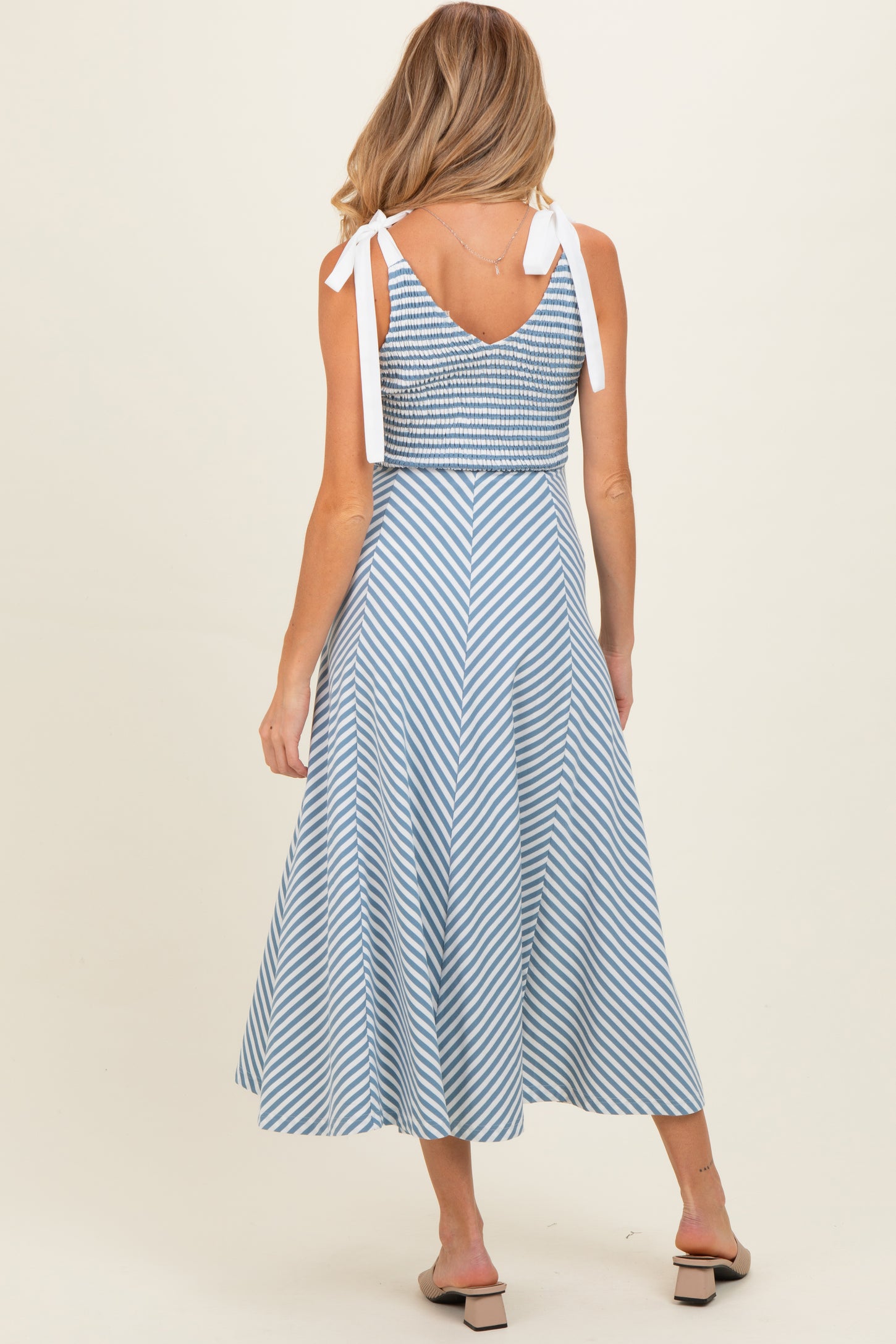 woman wearing a blue and white striped maternity dress with tie straps and a flared skirt, showing her back
