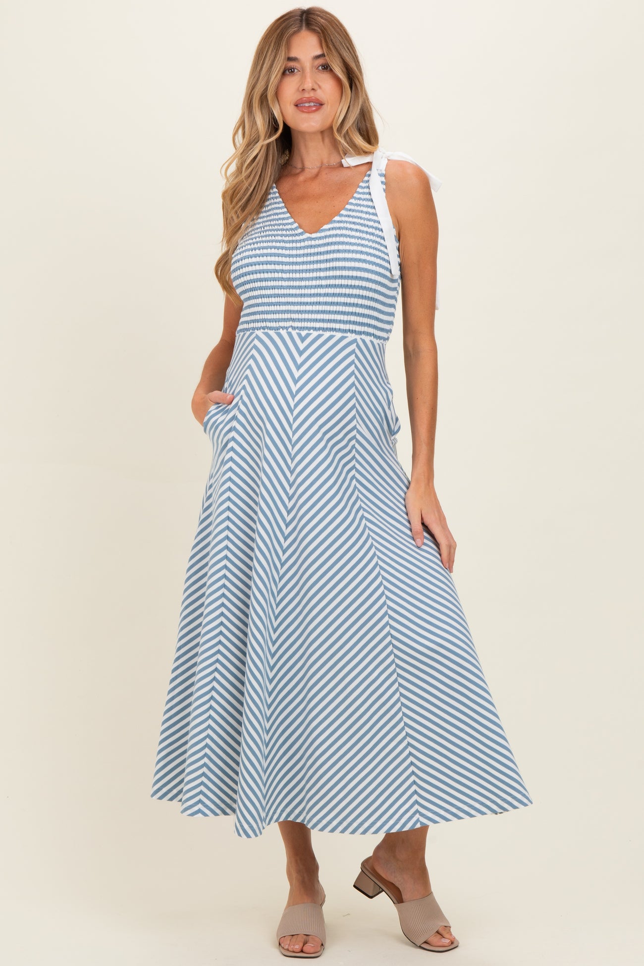 woman wearing a light blue and white striped maternity dress with a v-neck and shoulder ties, featuring pockets