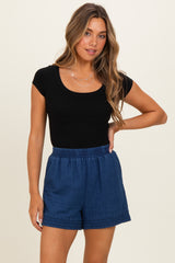 woman wearing a black scoop neck fitted top and blue relaxed fit shorts with a decorative hem